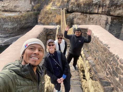       Group of people on a suspension bridge made of rope with surrounding cliff.
  