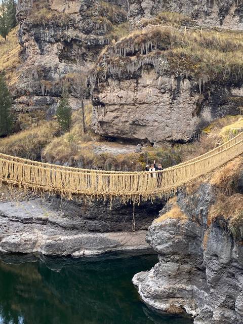       A suspension bridge made of rope hangs over a cliff with a few people crossing.
  