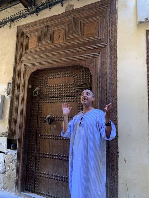       Man gesturing in front of a large wooden door.
  