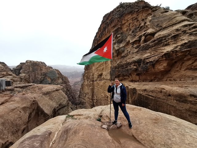 Person holding the Jordanian flag in a rocky area.