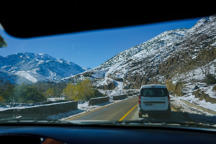 Snow-covered mountain road view from inside a vehicle.