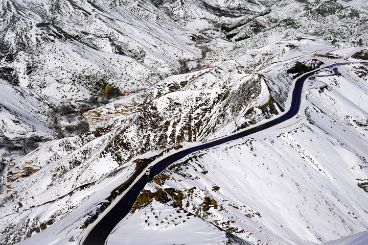 Aerial view of a winding road through snow-covered mountains.