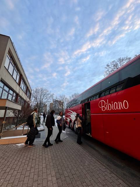 Tourists near a red tour bus on a snowy street.