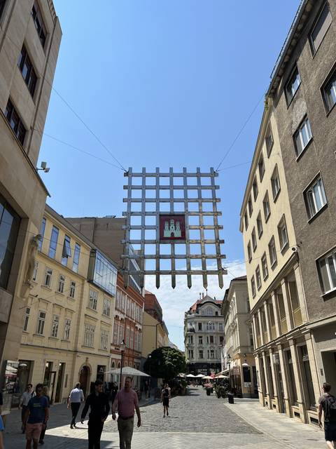 View down a street with grid-like decoration overhead.