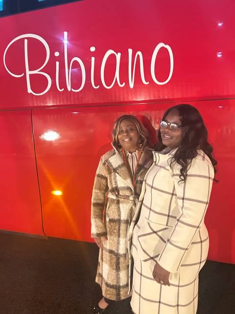       Two women posing in front of a bright red vehicle with text.
  