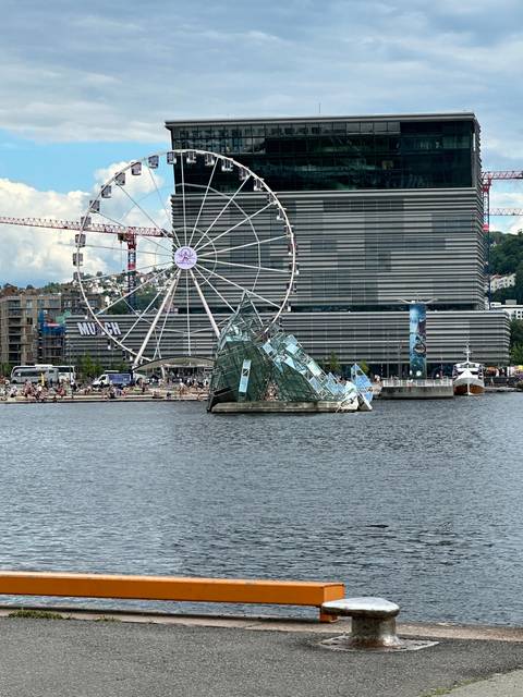       Ferris wheel and modern buildings by a waterfront.
  