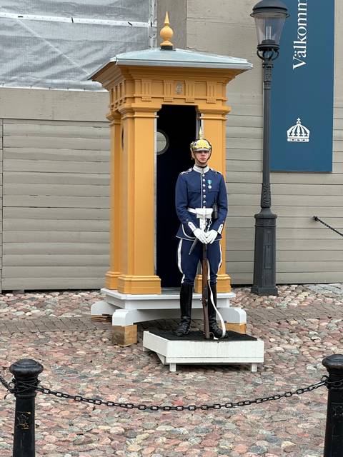       Guard standing in traditional uniform outside a building.
  
