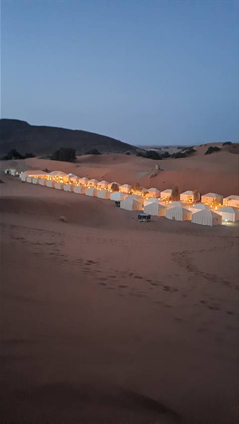 Row of lit tents in a desert at dusk.