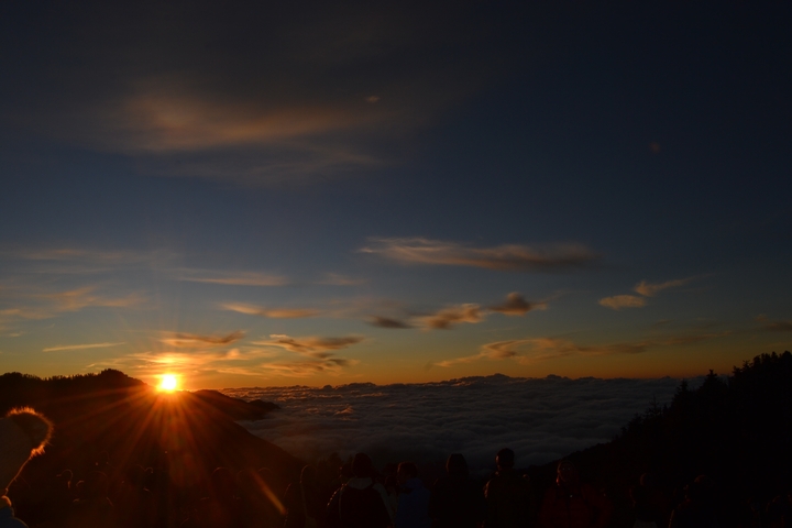 Sunset over rolling clouds with silhouettes of mountains.
