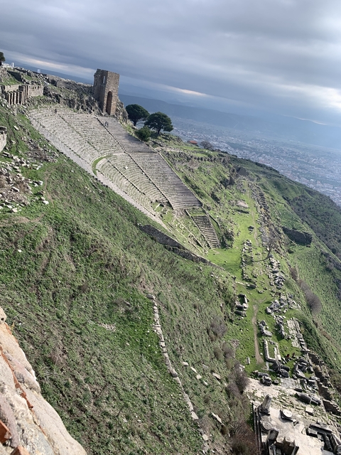Ancient theatre ruins on a hillside with a city in the background.