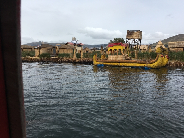       Traditional reed boat on a lake with reed houses in the background.
  