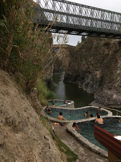       People relaxing in natural hot springs surrounded by canyon walls.
  