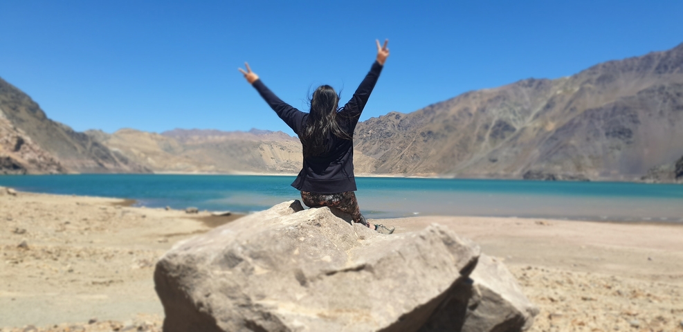 Person sitting on a rock with a lake and mountains in the background.