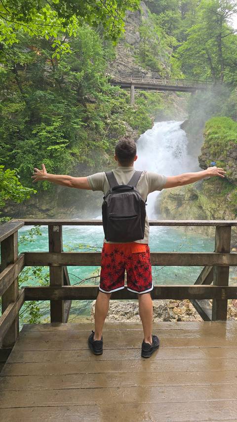 Person posing with arms outstretched in front of a waterfall.