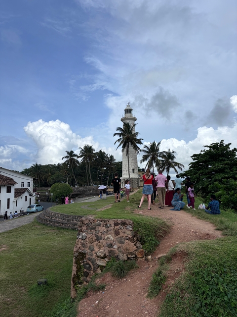       Lighthouse with people taking photos on a grassy path.
  