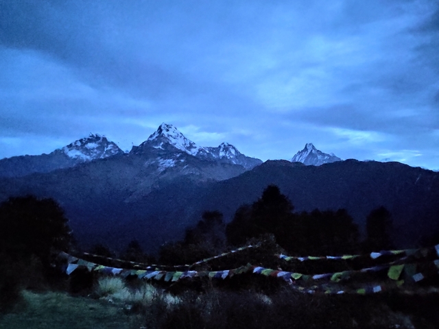       Snow-capped mountains under a twilight sky with prayer flags.
  