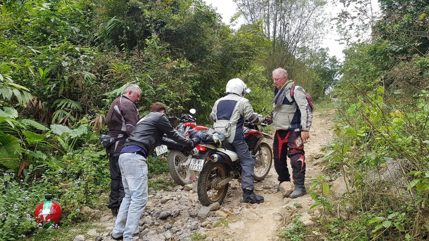 Bikers assisting each other on a rocky path.