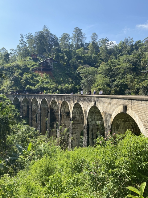       People walking on a bridge with arches in a scenic area.
  