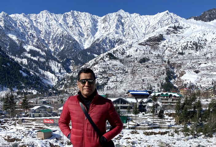 A man posing in front of snow-covered mountains and buildings.