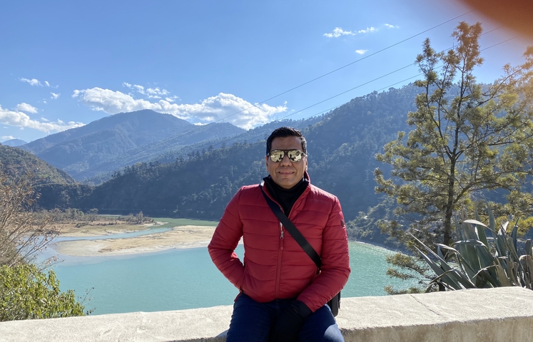 A man in a red jacket posing with a scenic mountainous backdrop.