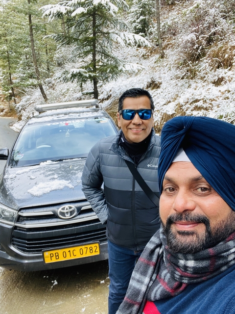 Two men taking a selfie with a car and snowy surroundings.