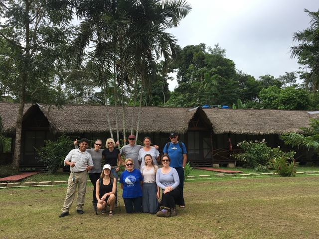       Group of people posing in front of thatched huts.
  