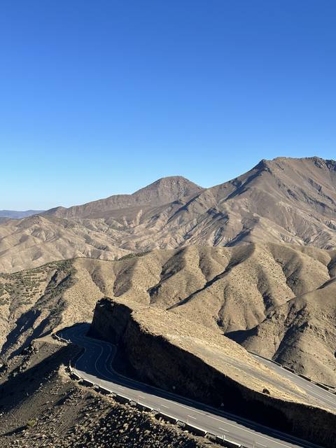 Road curving around mountain terrain with a clear sky.