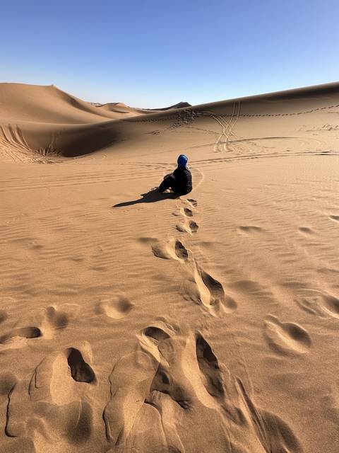 A person sitting on a sand dune in a desert landscape.