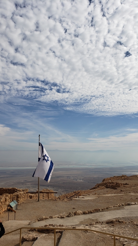 Israeli flag waving under a cloud-filled sky.
