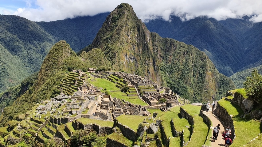       Panoramic view of Machu Picchu with terraces and green slopes.
  