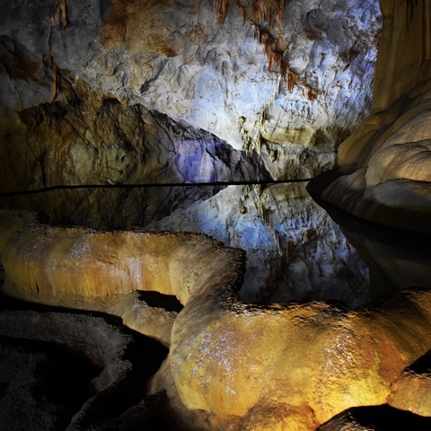       Stalactites and stalagmites in a cave with reflective waters.
  