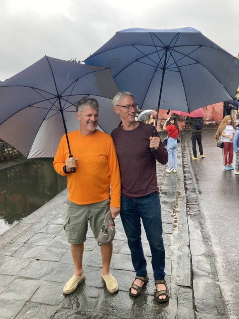       Two men with umbrellas standing on a walkway.
  
