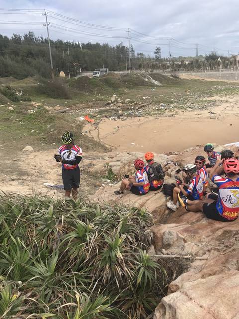 Cyclists resting on rocks by the beach.