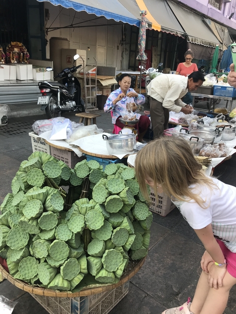 People at a market with lotus pods and food items on a table.