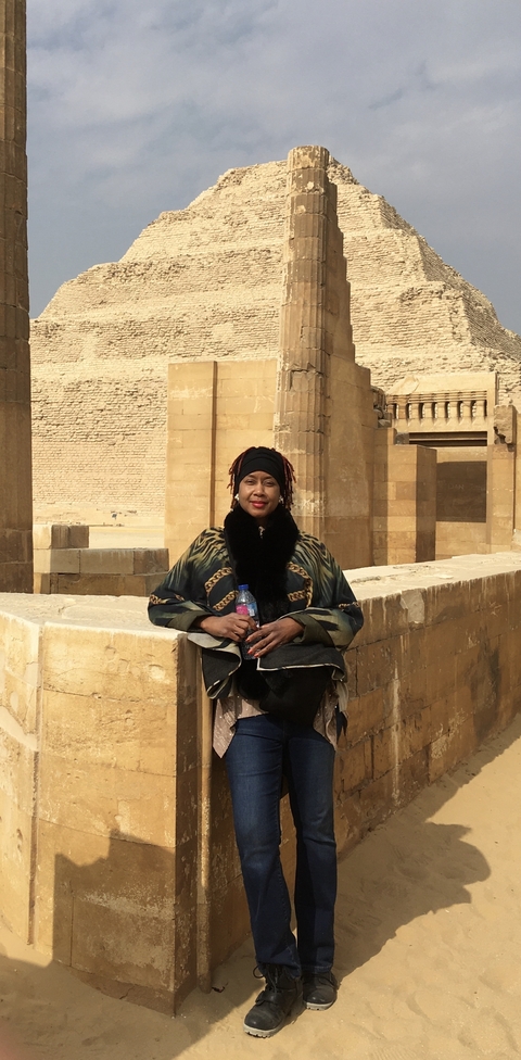       Person sitting by ancient stone structures under a bright sky.
  