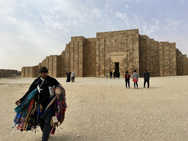       People exploring the ancient step pyramid in desert surroundings.
  