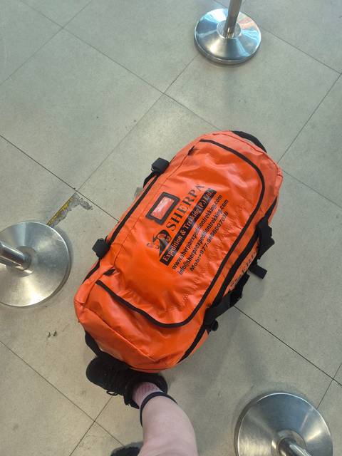       Orange sherpa bag with text resting on floor.
  