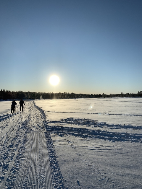 People walking across a snow-covered field in the sunlight.