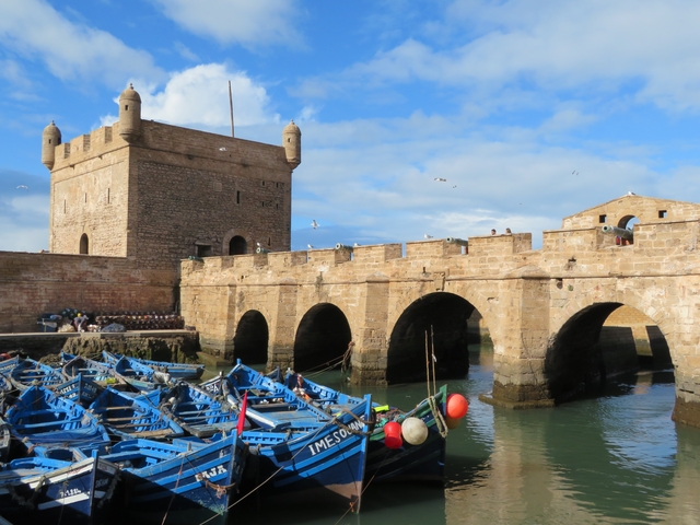 Historic fortified walls with boats floating in a Mediterranean harbor.