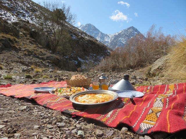 A Moroccan meal laid out on a colorful rug with mountains in the background.