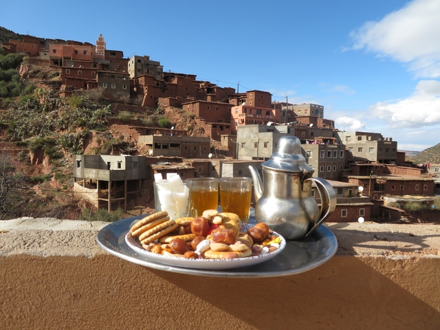 Traditional Moroccan treats and tea with a view of a village on a hill.