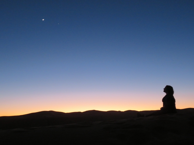 Silhouette of a person meditating against a sunset in a desert.