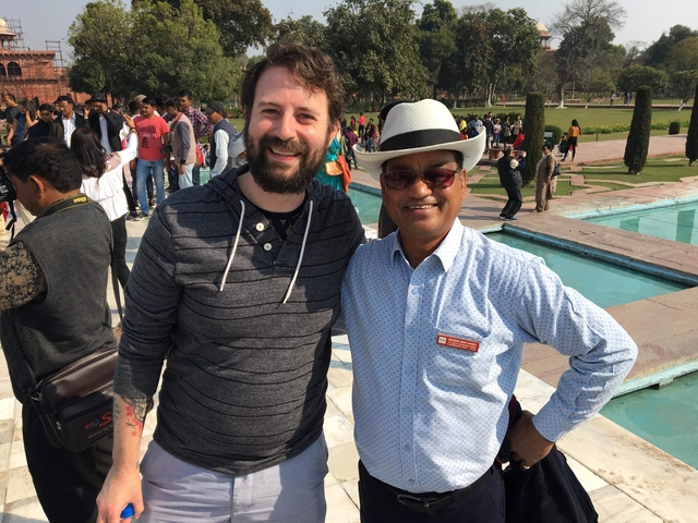       Two men posing happily in a busy public area with a fountain.
  