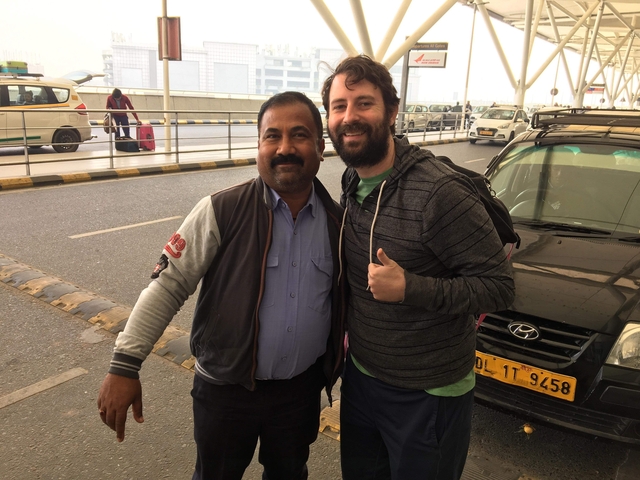       Two men posing happily in front of a car at the airport.
  