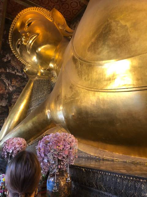       Reclining Buddha statue with floral arrangement.
  
