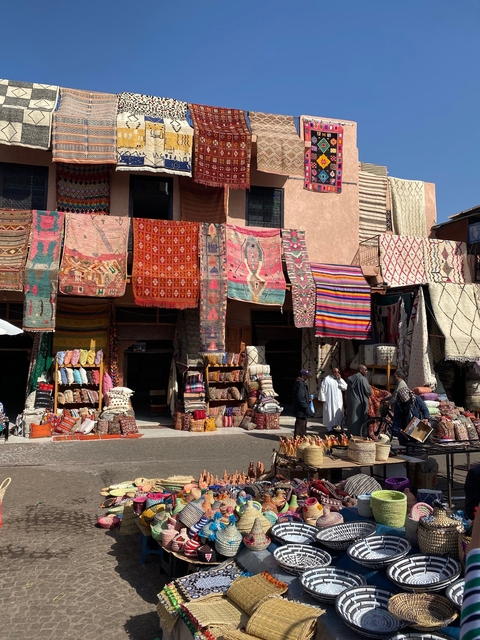       Traditional Moroccan market with rugs and people shopping.
  
