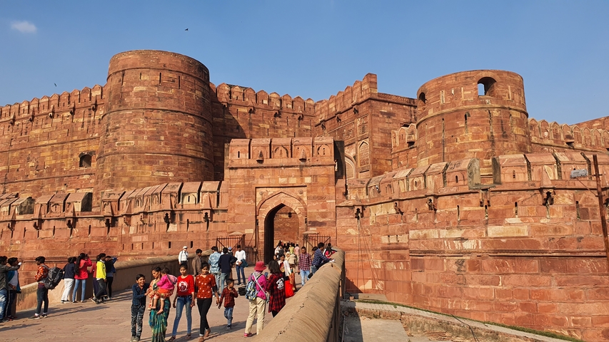 A large red fort with people entering through the main gate.