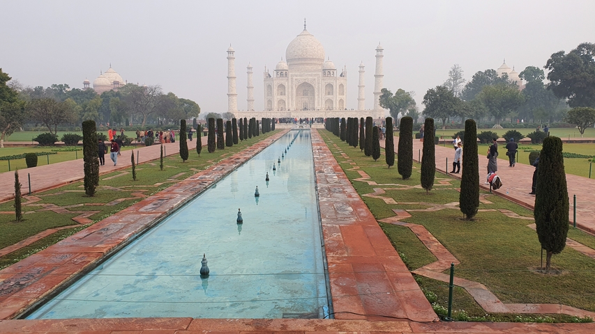 The Taj Mahal with its reflection in the water and people in the gardens.