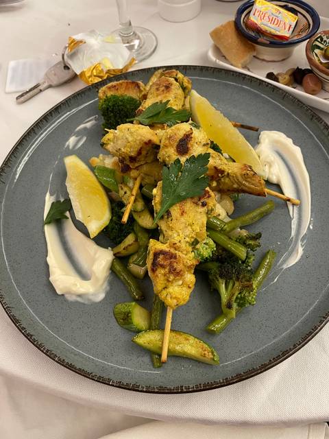       A plate of grilled chicken skewers with vegetables and sauces.
  