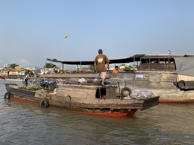       Man standing on a small boat in a floating market setting.
  